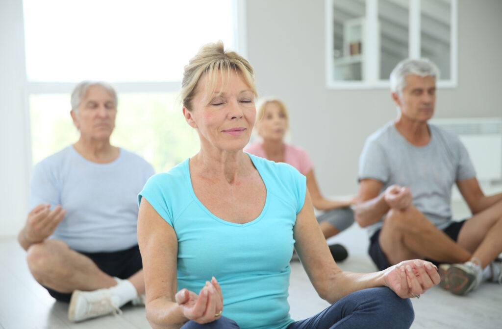 A group of seniors with closed eyes practicing yoga and are sitting on yoga mats.