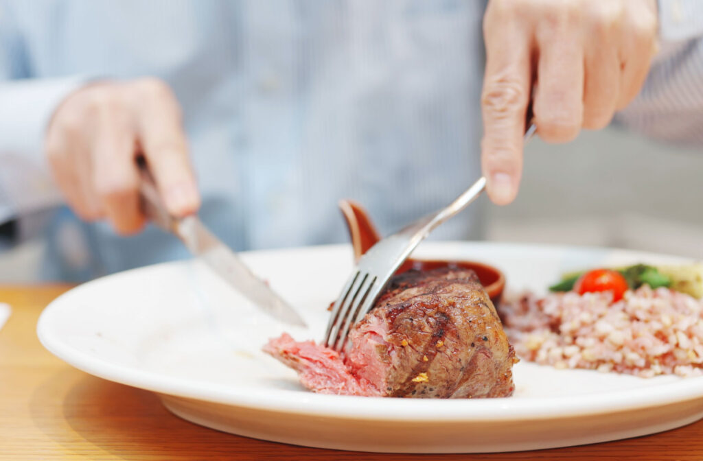 Close up of a senior man’s hand cutting a grilled steak with rice on the side of the plate