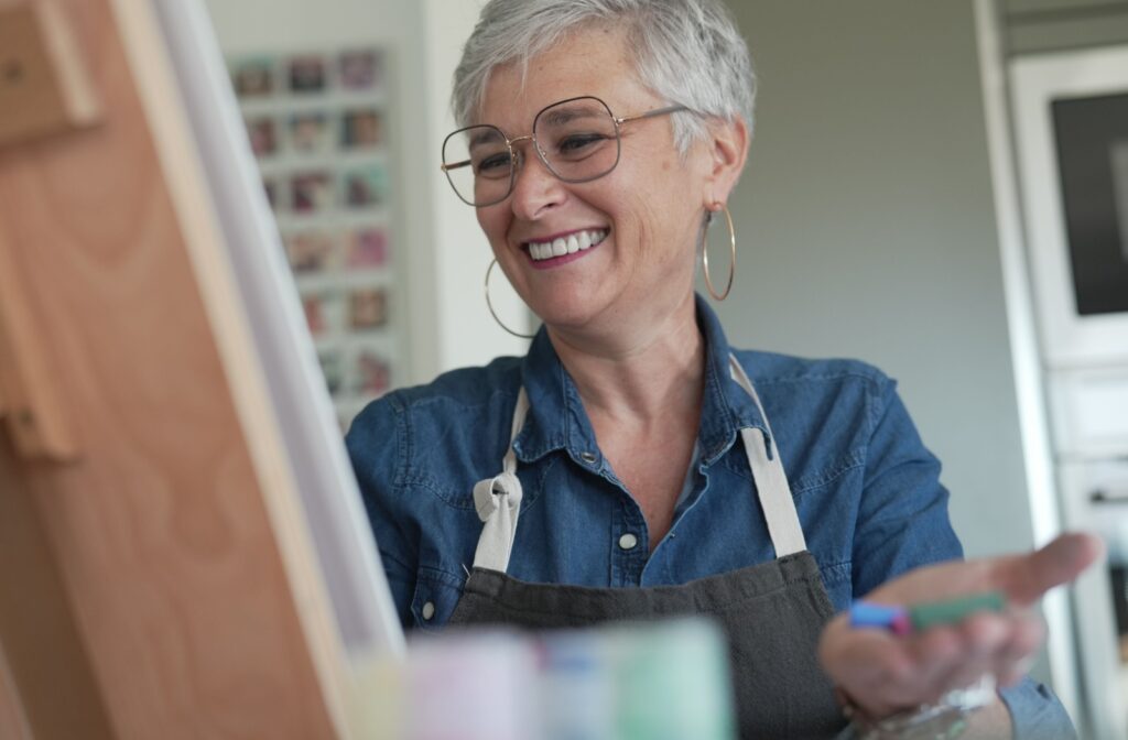 A close-up image of a senior woman smiling while painting on an easel during arts and crafts.