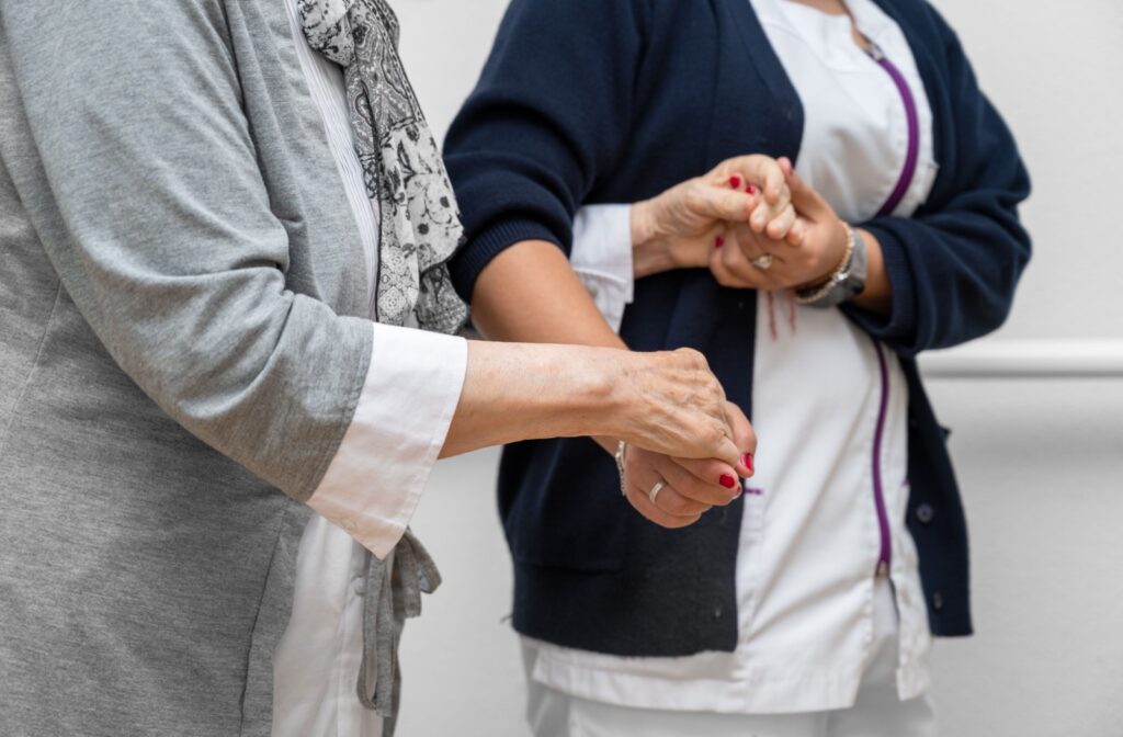 A close-up image of a staff member in assisted living helping an older adult walk.