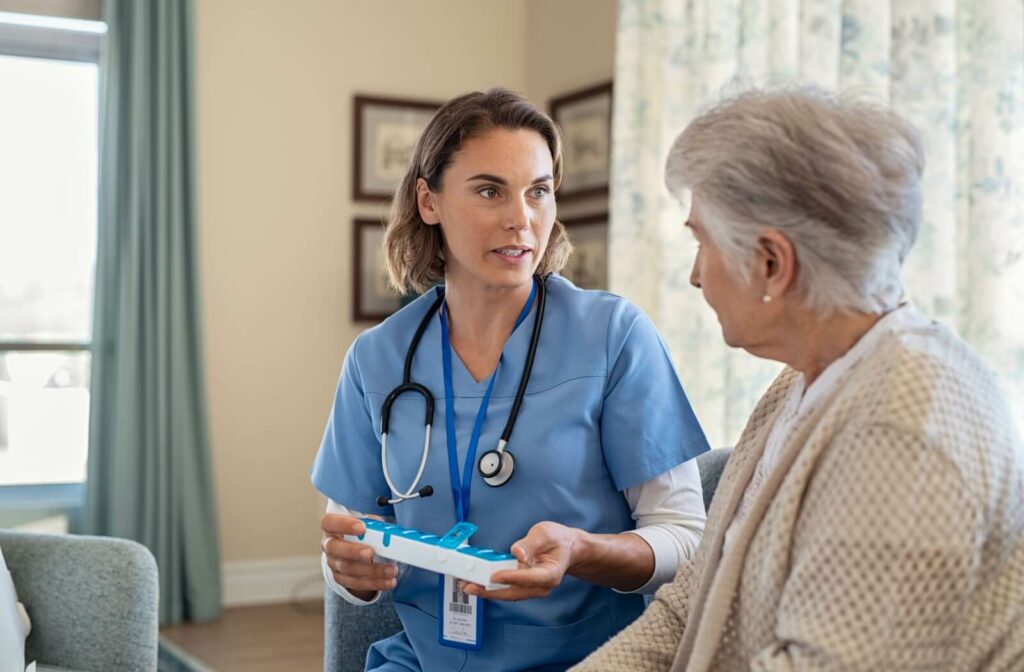 A medical staff member in assisted living holding a pill organizer and discussing medication dosage with an older adult.