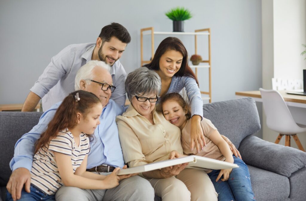 A senior couple is visiting with their adult child and grandchildren. They all sit on the couch and look at family photo albums.
