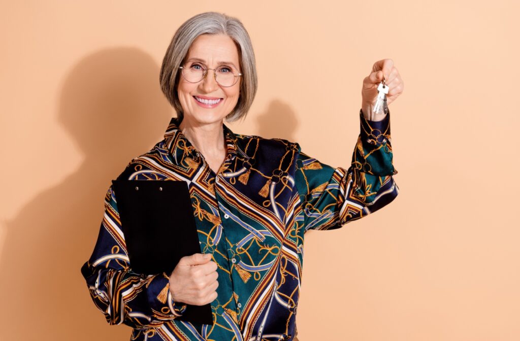 A smiling older woman holds up a set of keys to their new assisted living home, holding a moving checklist in the other hand