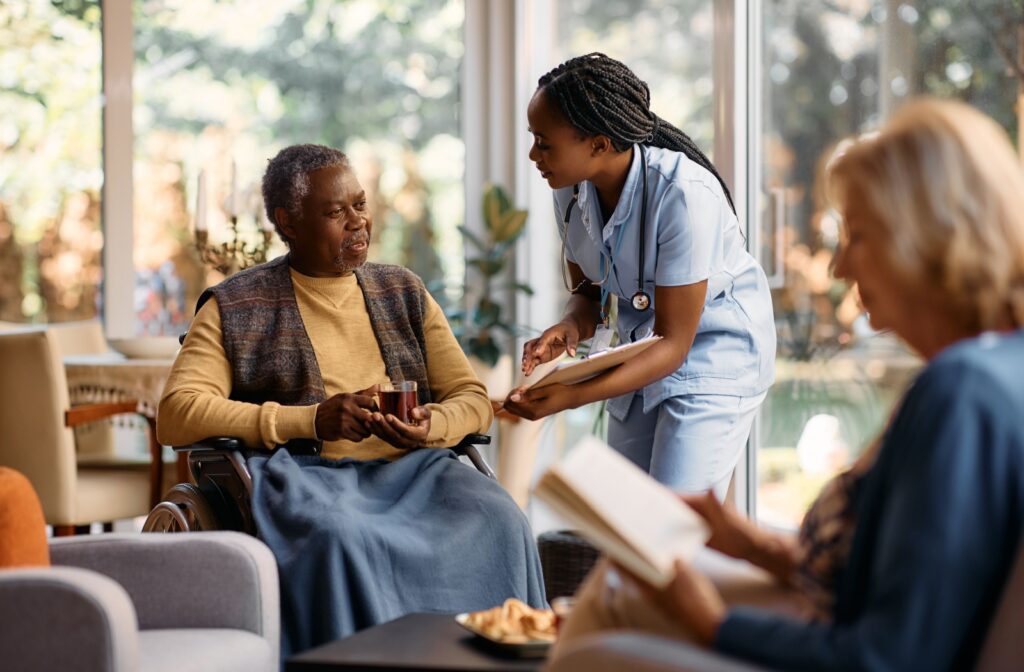 A nurse checks in on a senior in a communal area of their assisted living home to see if they need help with medications