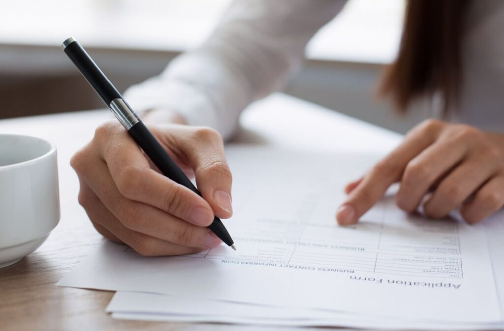 Close-up of a hand holding a pen of an adult completing an application form for their loved one for assisted living.