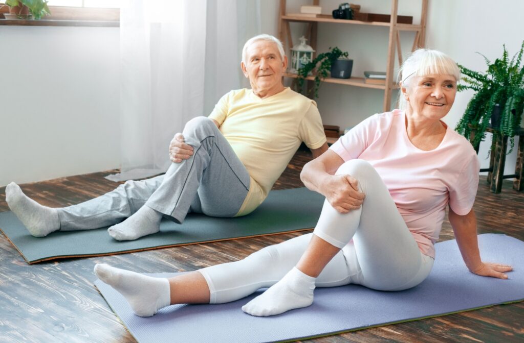 Two older adults lying on yoga mats twist to one side to strengthen their hips and reduce their symptoms of osteoporosis