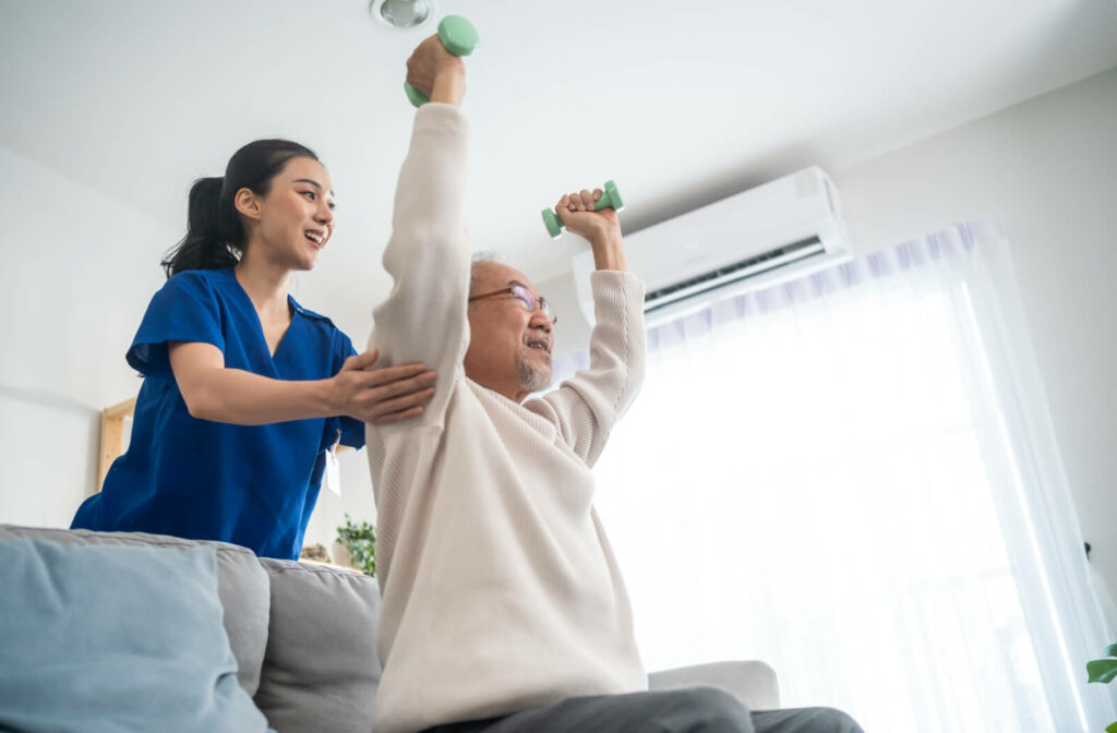 A caregiver in assisted living helps an older resident lift small weights overhead to strengthen their arms against osteoporosis