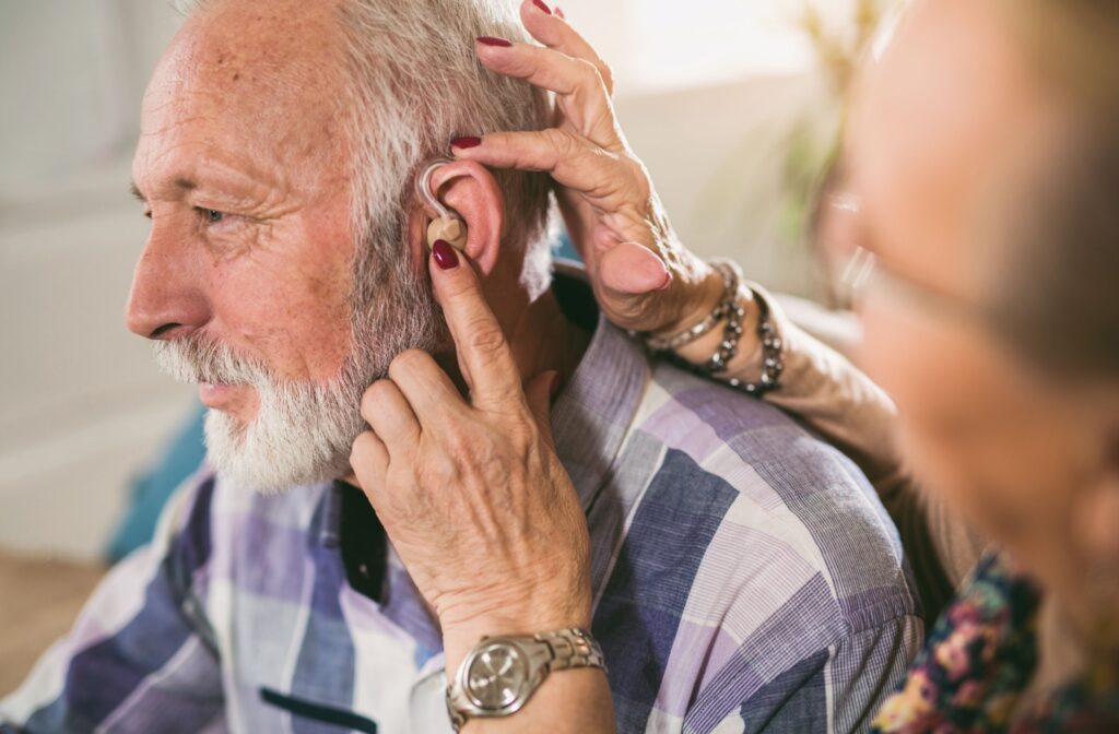 An elderly man getting hearing aids put on by his wife.