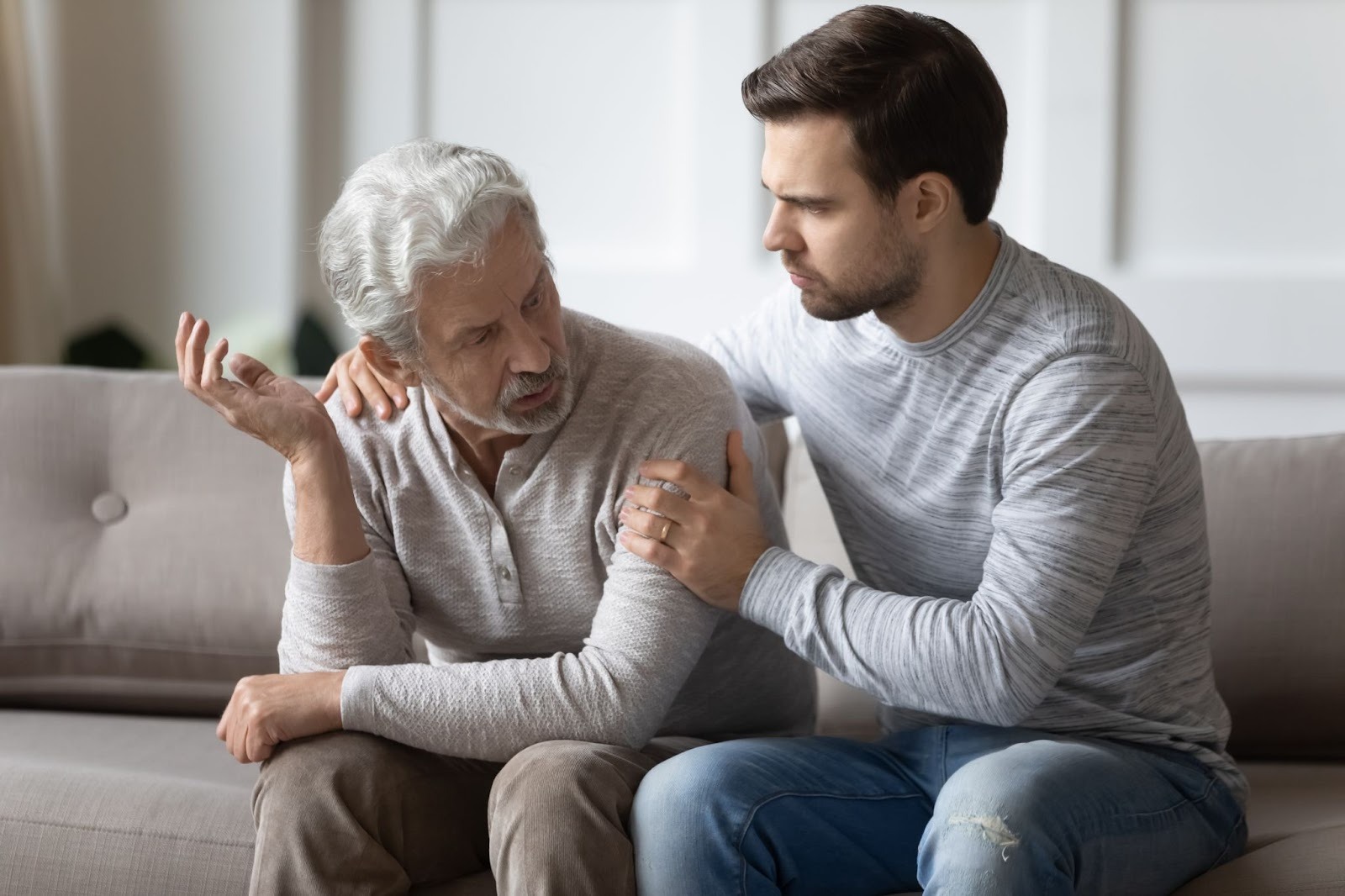 An adult child gently puts their arms around their distressed senior parent to offer support during an important conversation.