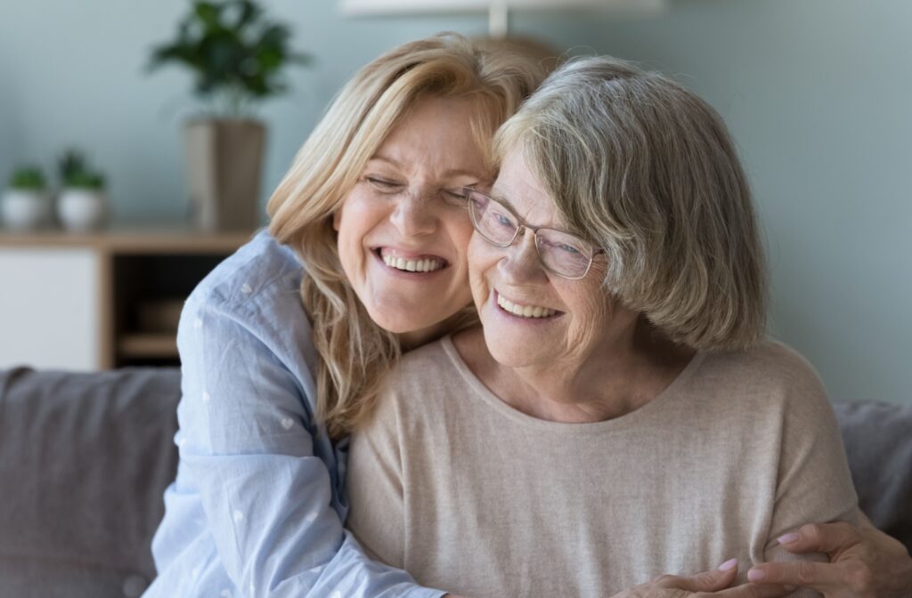 An adult smiles as they embrace their smiling senior loved one