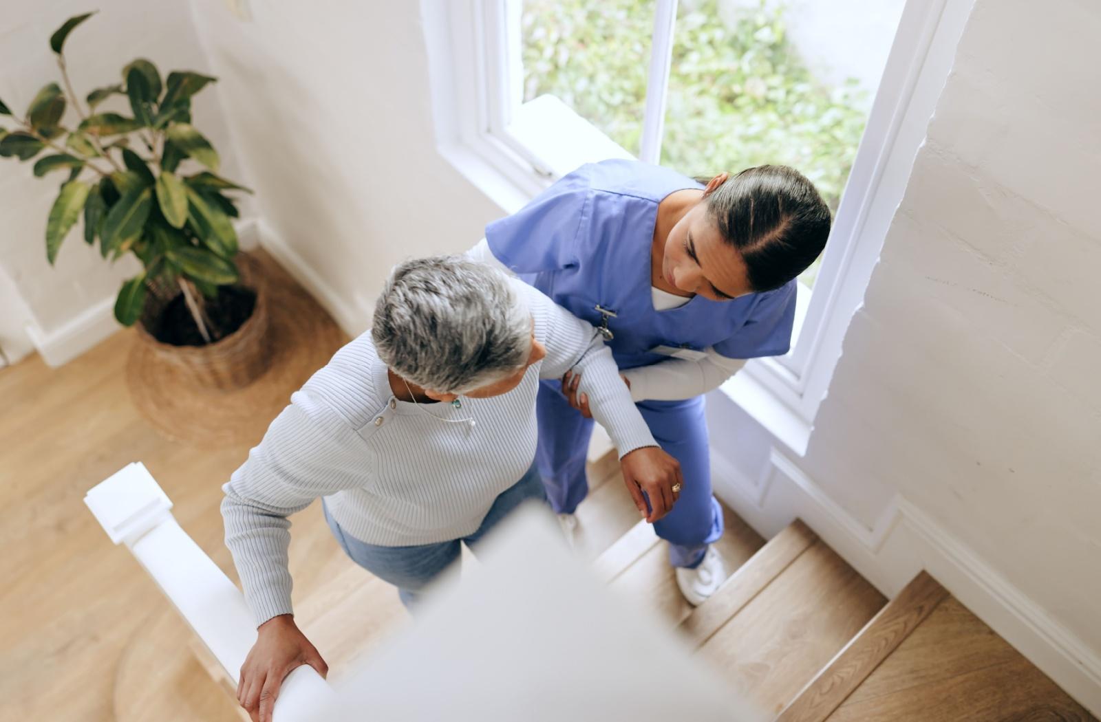 a carer helps a senior up the stairs
